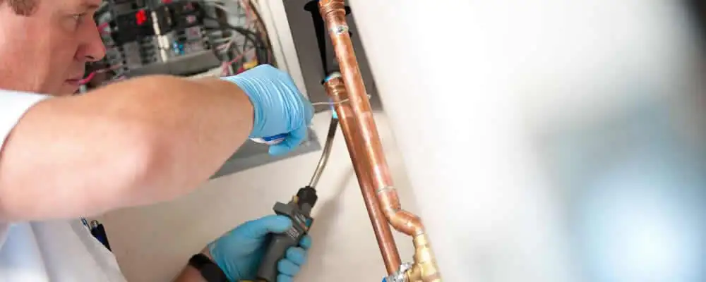 Water heater repair technician testing copper pipe connections and controls in Dallas, TX